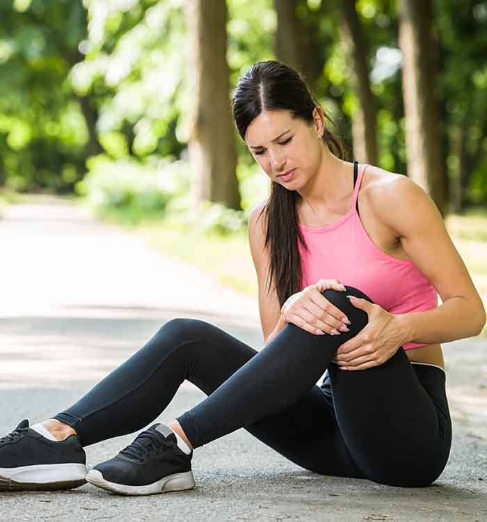 Woman experiencing knee pain while exercising outdoors