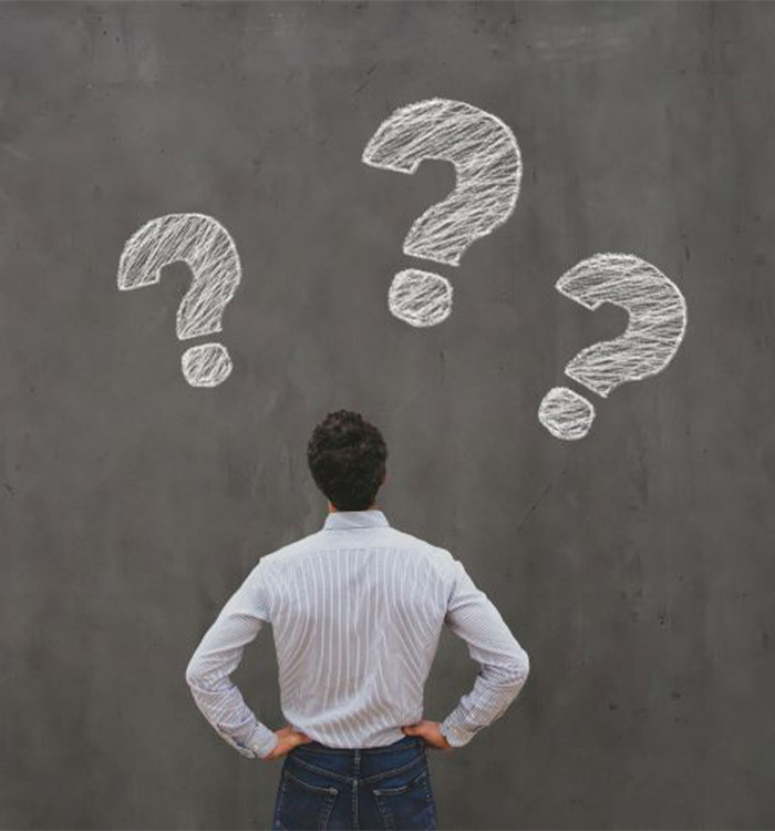 Man looking at chalkboard that has three question marks drawn on it