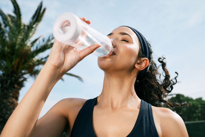 Woman standing outside, sipping from water bottle